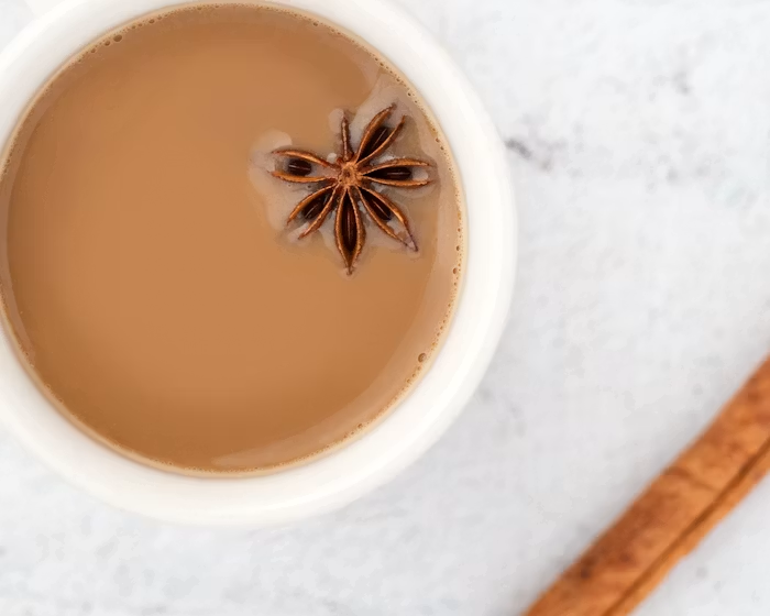 A warm cup of masala chai with a star anise pod and a cinnamon stick resting on a marble surface